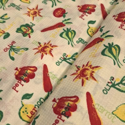 בד פיקה דק ועדין בצבע שמנת בהדפס שמש וירקות בגווני אדום, ירוק וצהוב.